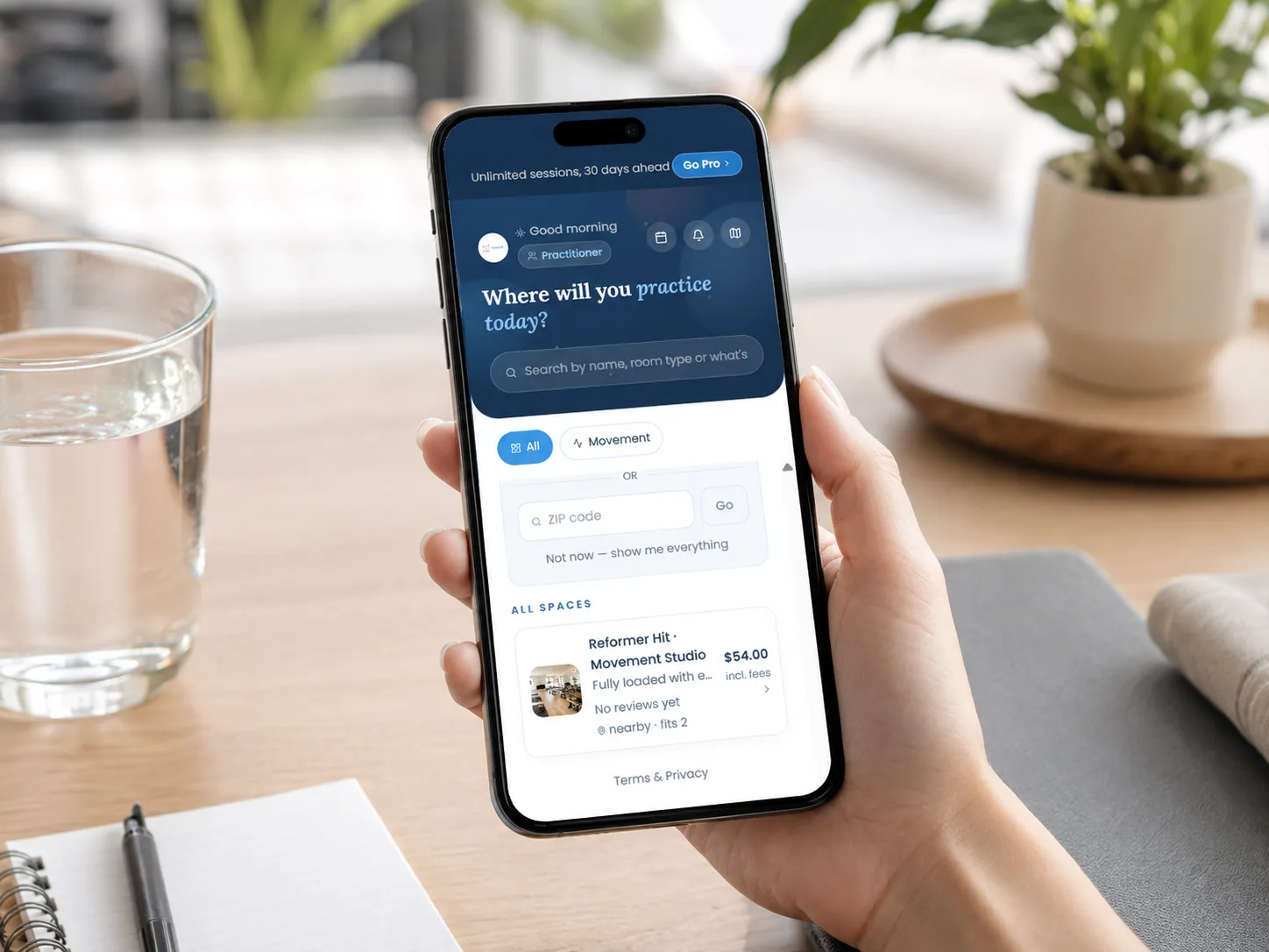 A hand holding a phone showing the app: a search for a room, and a movement studio listed at $54.00 an hour including fees.
